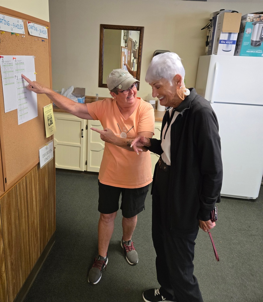 one lady pointing at board on wall another lady laughing