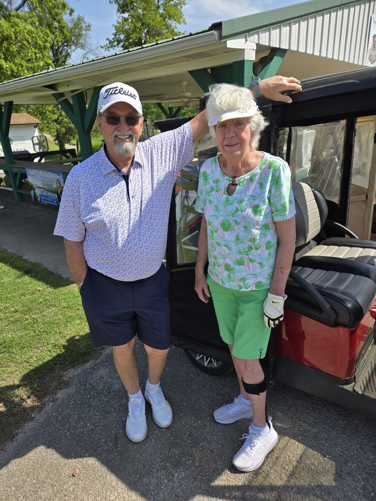 A man and woman standing next to golf cart