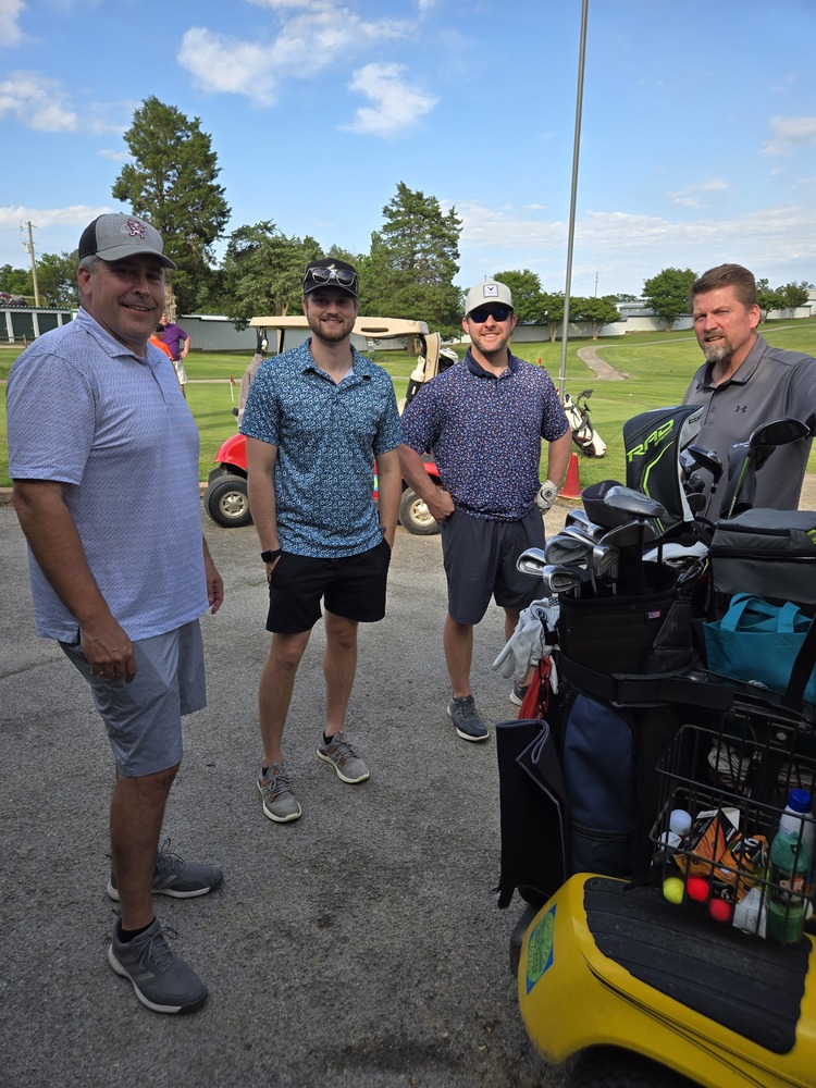 4 men standing behind a golf cart.