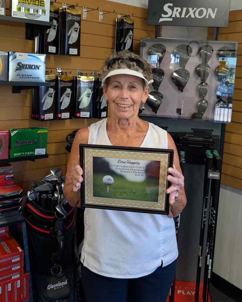 Elder lady in golf shop wearing white visor and holding a certificate
