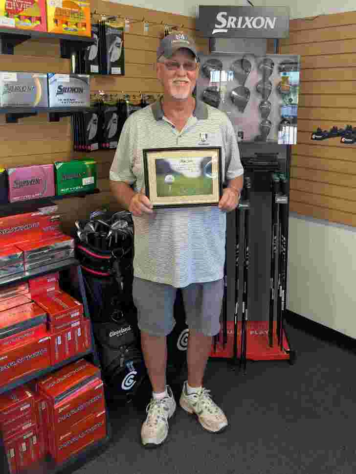 Man wearing ball cap holding certificate standing in golf shop