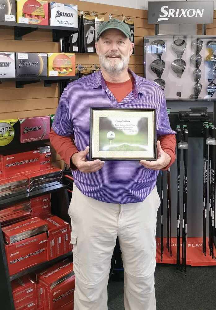 Man with purple shirt and cap holding certificate in golf shop